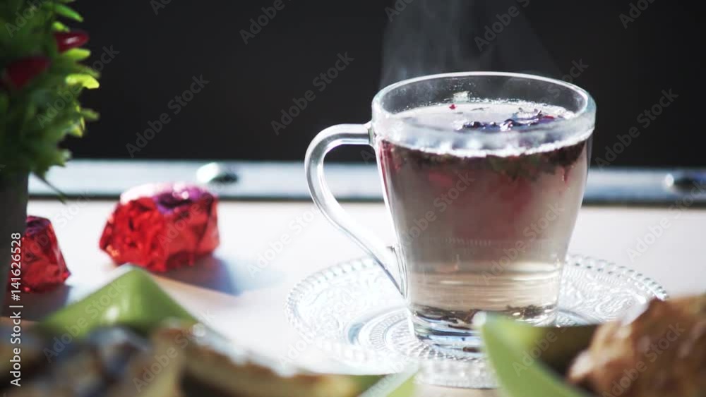 Making hot tea in the kitchen. Pouring boiling water into the glass cup with tea leaves and herbs at the bottom. Time for tea break. Breakfast, relax, morning, meditation concept.