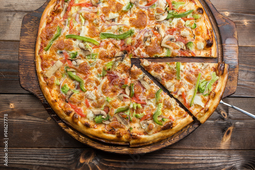 Delicious pizza with mushrooms - thin pastry crust isolated at wooden background on wooden desk