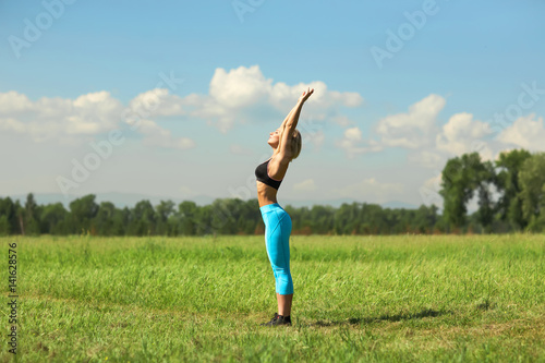 Beautiful sport woman doing stretching fitness exercise in city park at green grass. Yoga postures