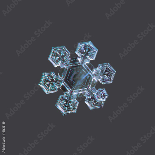 Real snowflake macro photo: medium size snow crystal of star plate type with six short, broad arms and big central hexagon with simple inner pattern. Snowflake isolated on uniform gray background.