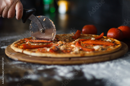woman's hand with a knife cut the pizza on black background close-up.