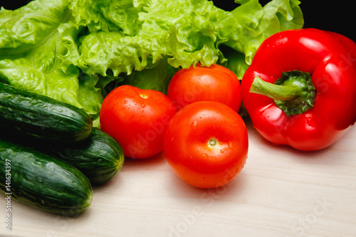 Fresh vegetables on the table: red pepper, lettuce, cucumber, tomatoes, sheet for notes - notepad. Cutting board