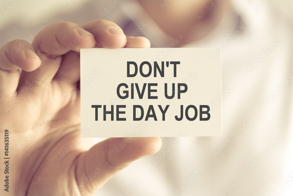 Businessman holding DONT GIVE UP THE DAY JOB message card Businessman holding DONT GIVE UP THE DAY JOB message card