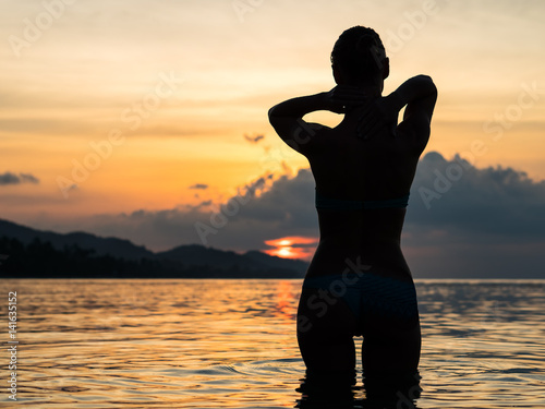 Woman is standing in the sea and watching the sunset  