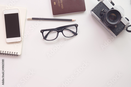 Flat lay design of work desk with notebook, glasses, camera, smartphone and passport on white background.