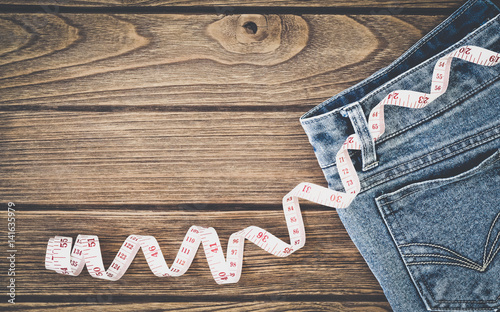 Weight loss concept, Blue jeans and measuring tape on wooden background, Top view with copy space