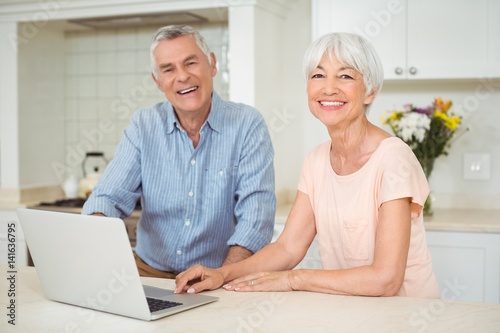 Portrait of senior couple using laptop in kitchen