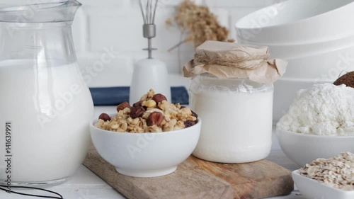 Piece of kitchen interior. Dairy products, eggs, cereals, on wooden table - milk, cottage cheese, sour cream, yoghurt, granola, muesli. Concept of healthy eating. Slow pan.