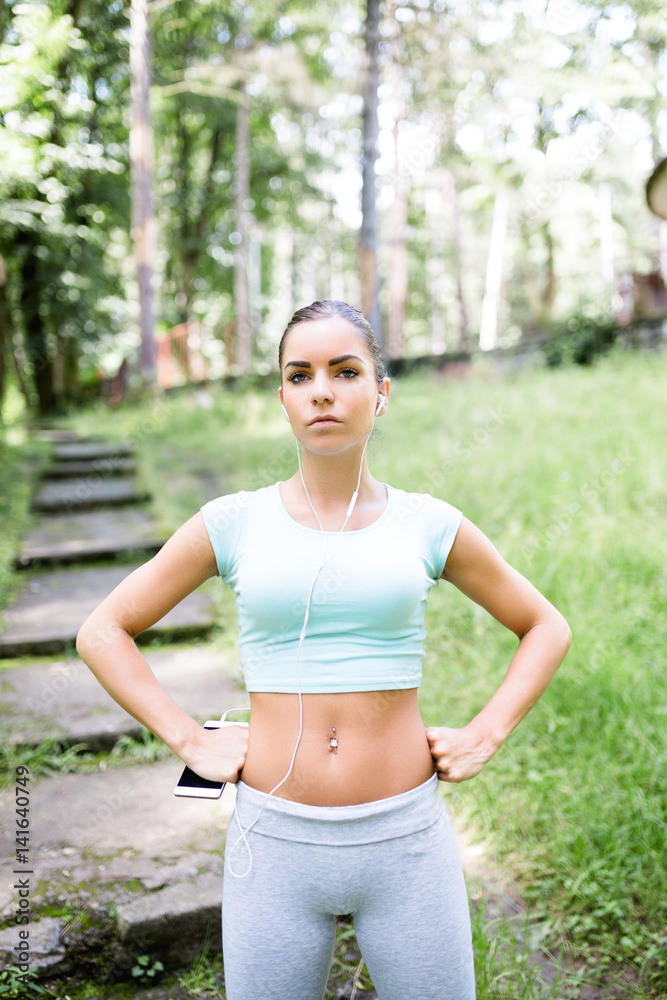 Attractive young woman with sunglasses resting in city park after fitness activity and listening to music on her smart phone. Attractive young woman with sunglasses resting in city park after fitness activity and listening to music on her smart phone.