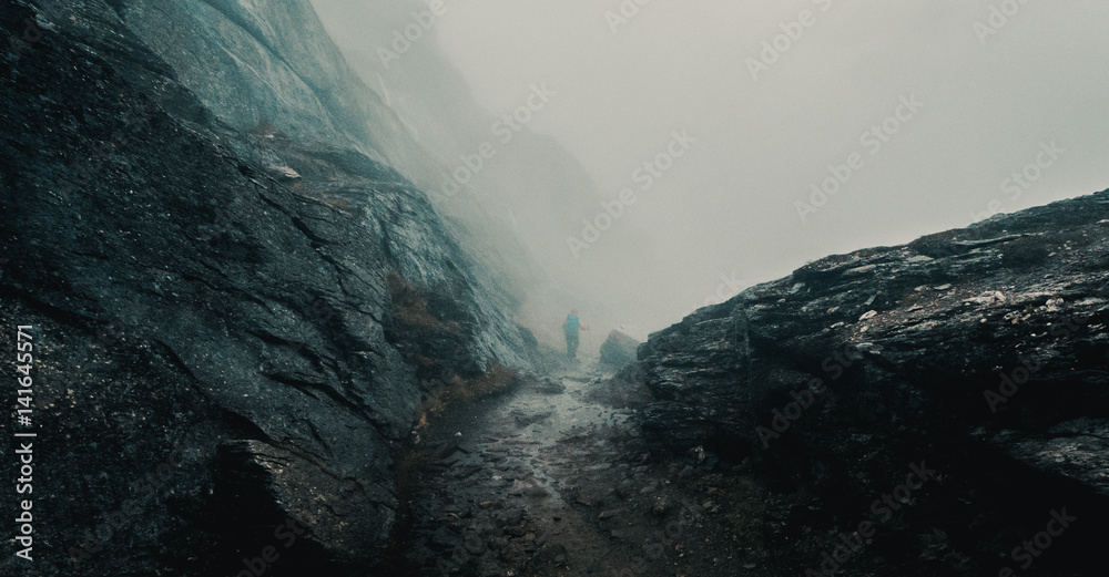 Hiker hiking in foggy mountain trail. Trolltunga, Norway.