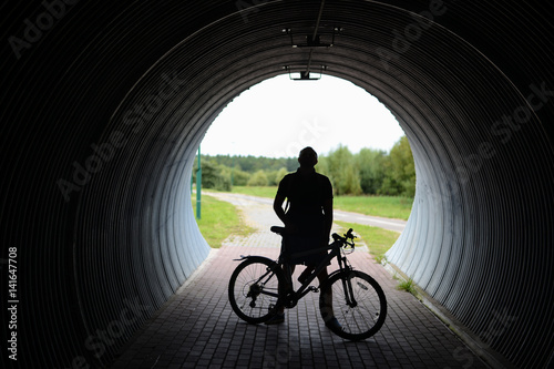 Man cyclist stands on the bike path under the bridge