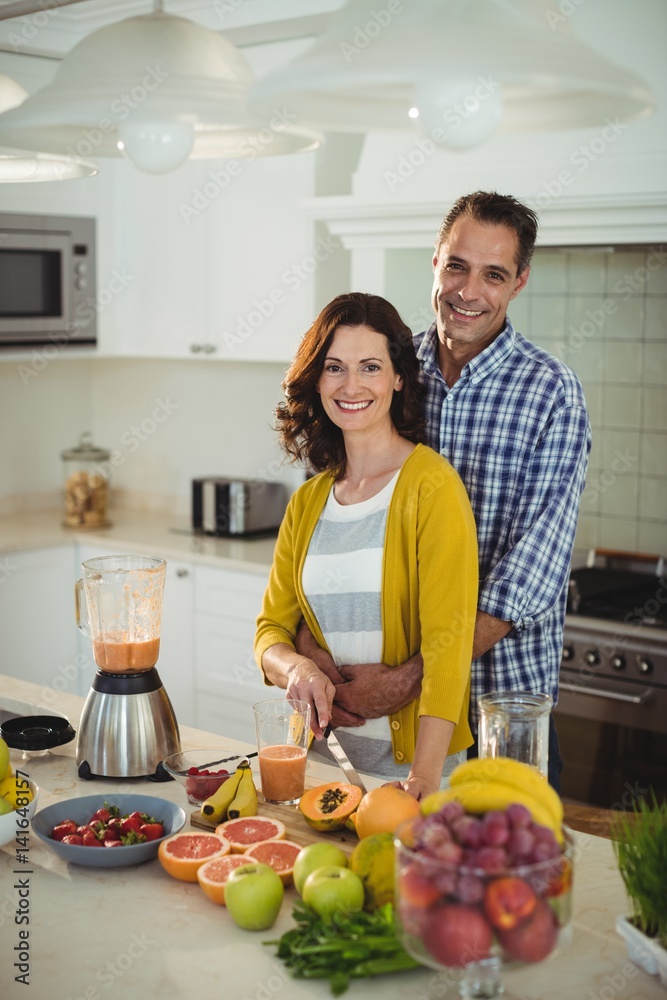 Happy couple embracing while preparing smoothie in kitchen