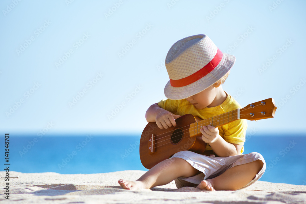 Fototapeta premium Little boy plays guitar ukulele at sea beach