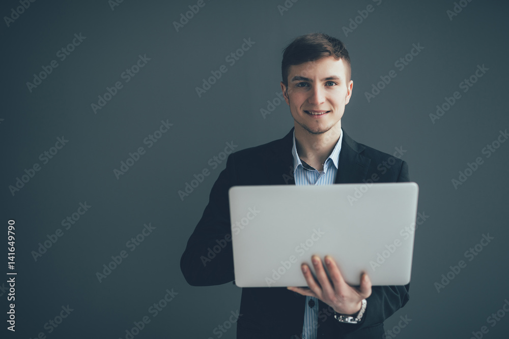 Handsome young businessman is using a laptop, looking at camera and smiling, on black background Handsome young businessman is using a laptop, looking at camera and smiling, on black background