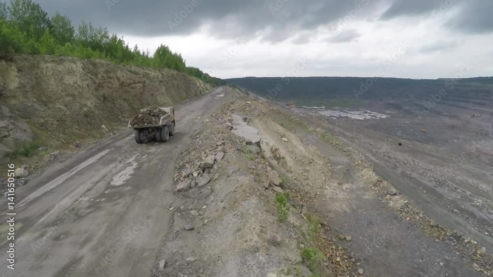 Loaded quarry dump truck with a full body of stones stands on a road near the edge of the quarry. Shooting from the drone from the air, the camera moves to the side. Storm clouds and a giant bat. Loaded quarry dump truck with a full body of stones stands on a road near the edge of the quarry. Shooting from the drone from the air, the camera moves to the side. Storm clouds and a giant bat.