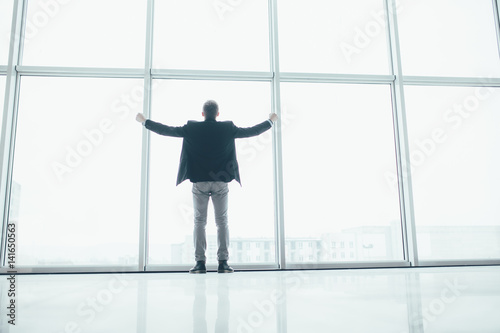 Stylish business man in rised hands victory in the background of a large window