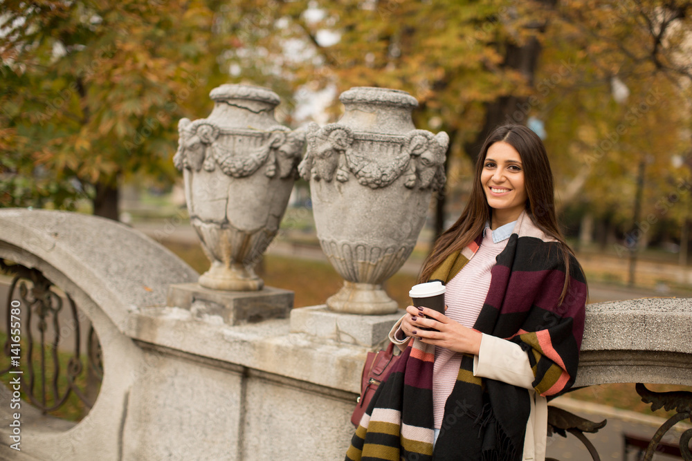 Fototapeta premium Woman standing outside, drinking coffee to go and holding a mobile phone in hand
