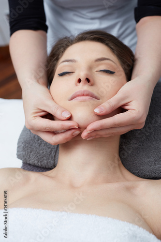  Relaxing beautiful woman having a massage for her skin on a face in beauty salon 