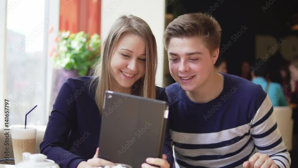 Young attractive couple using digital tablet computer, looking at the screen in cafe. Young attractive couple using digital tablet computer, looking at the screen in cafe.