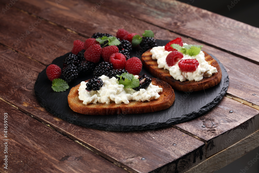 Bread with cheese cream and blackberries and raspberries for lunch table. Sharing antipasti on party or summer picnic time over wooden rustic background. Bread with cheese cream and blackberries and raspberries for lunch table. Sharing antipasti on party or summer picnic time over wooden rustic background.