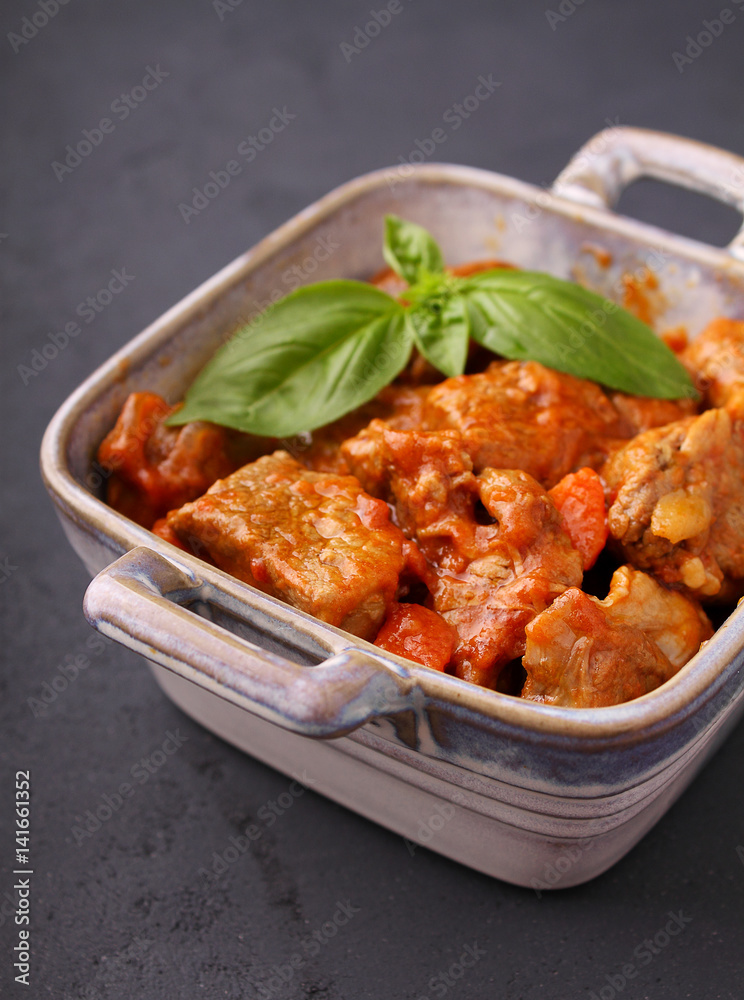 Ragout of meat with onions, carrots and tomatoes, decorated with basil,