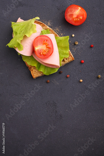 sandwich with doctoral sausage with lettuce and tomato. black bakground