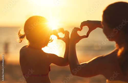 The concept of love, parenthood and happy family. Mother and child daughter show heart from hands at sunset