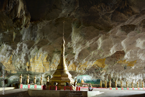 Young girl sitting in meditation in Sadan Cave, Myanmar. View of the big golden pagoda and row of the statues of buddhist monks. photo