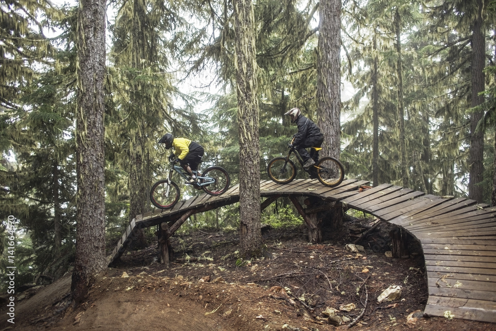 Friends riding mountain bikes on boardwalk in forest Friends riding mountain bikes on boardwalk in forest