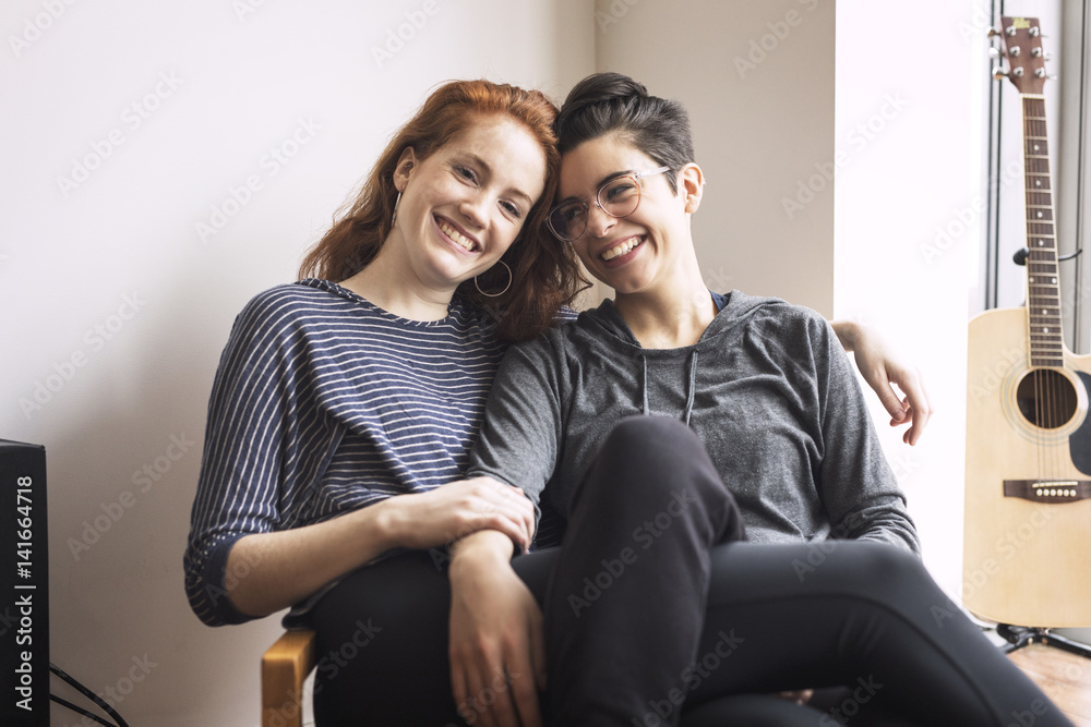 Happy lesbian couple sitting on chair at home Happy lesbian couple sitting on chair at home