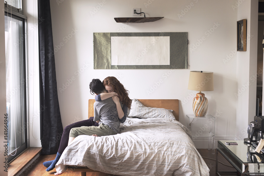 Lesbian couple embracing each other while sitting on bed at home Lesbian couple embracing each other while sitting on bed at home