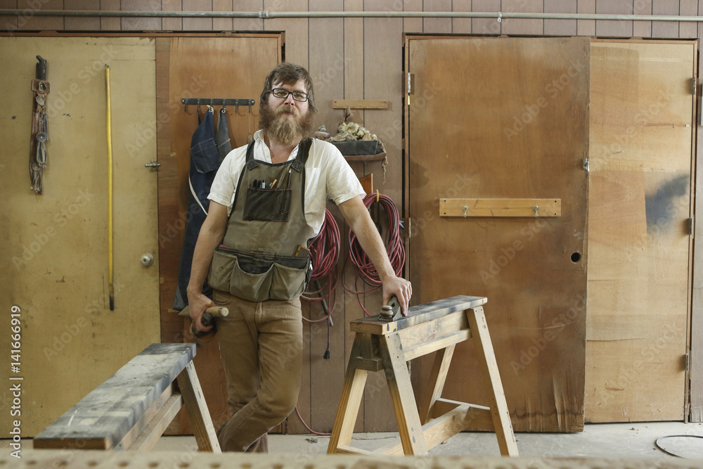 Portrait of confident carpenter with work tools standing in workshop Portrait of confident carpenter with work tools standing in workshop
