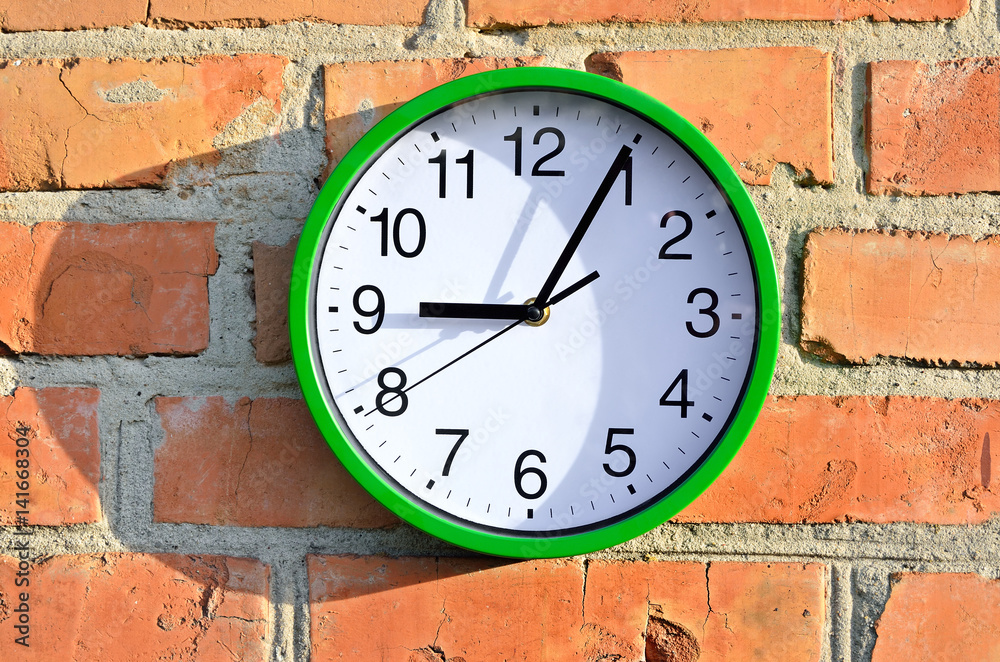 Green wall clock hanging on a brick wall