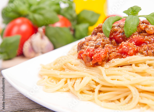 Spaghetti bolognese,some tomatoes, olive oil, basil, garlic, and raw pasta in the background