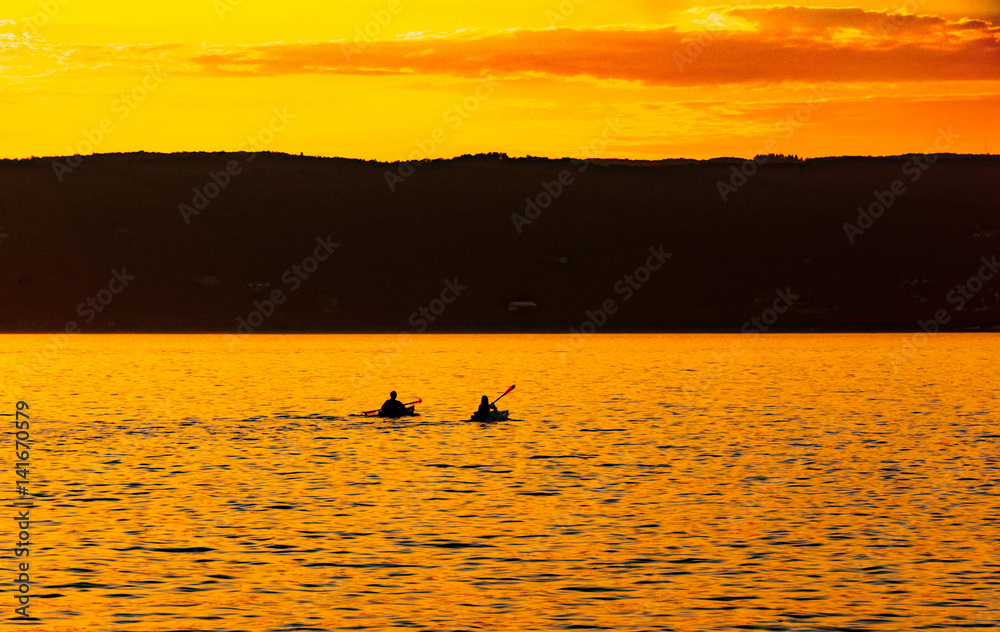Fototapeta premium Kayakers paddle on Lake Superior against a vibrant golden sunset