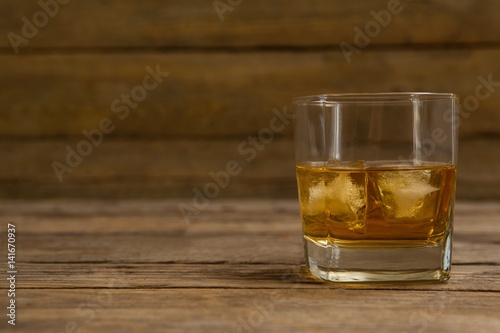 Glass of whisky with ice cube on wooden table