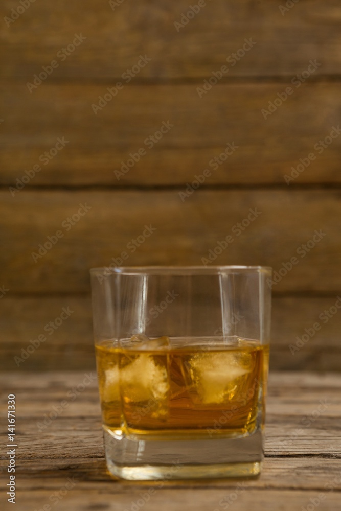 Glass of whisky with ice cube on wooden table Glass of whisky with ice cube on wooden table
