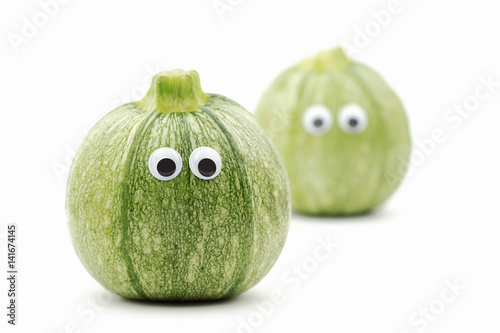 two round zucchini with googly eyes on white background - funny food