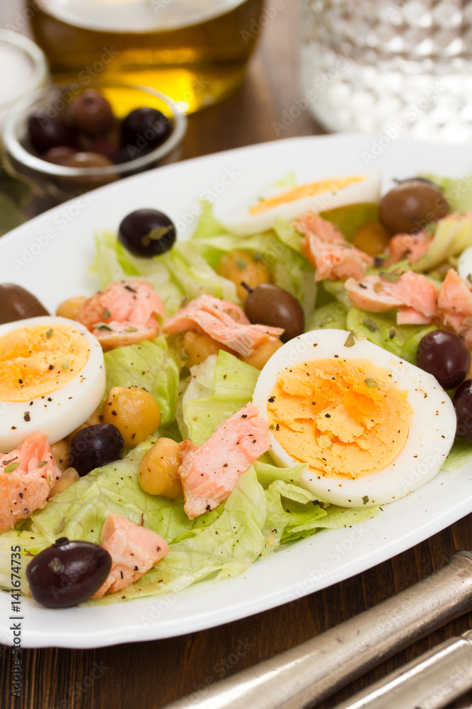 salad with salmon, eggs and olives on white dish