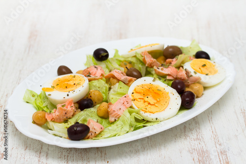 salad with salmon, eggs and olives on white dish