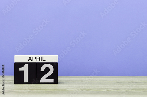 April 12th. Day 12 of month, calendar on wooden table and purple background. Spring time, empty space for text