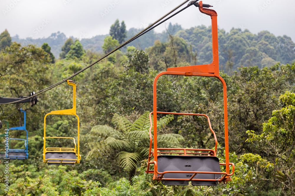 Orange, yellow, and blue chairs on the ski lift at the Recinto del Pensamiento nature reserve near Manizales, Colombia. Orange, yellow, and blue chairs on the ski lift at the Recinto del Pensamiento nature reserve near Manizales, Colombia.