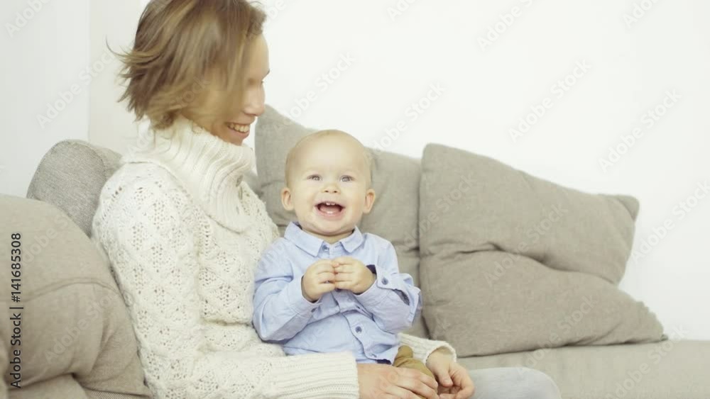 Portrait of happy mother and son sitting on sofa at home, smiling and laughing, looking straight ahead Portrait of happy mother and son sitting on sofa at home, smiling and laughing, looking straight ahead