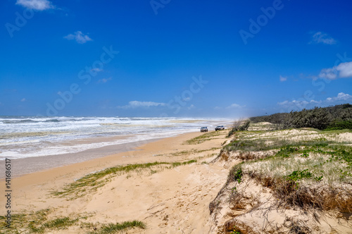 Stunning view of 75 Mile Beach on Fraser Island  Queensland  Australia  located in the Great Sandy National Park. Rough ocean on a sunny day  two four wheel drive cars in the background.