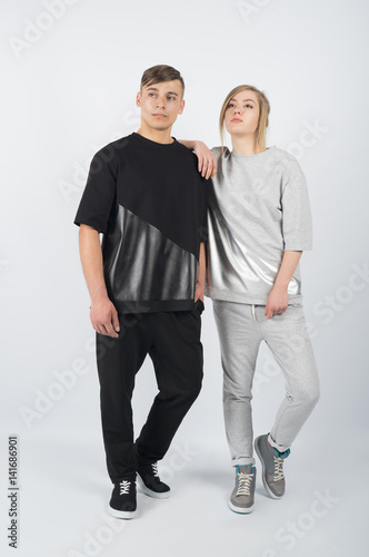 Fashion girl leans on boy's shoulder. Young muscular man wearing black clothes and sneakers with girl in grey clothes solated on white background