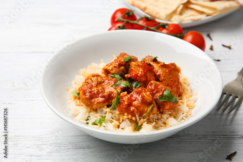 Vászonkép Plate with tasty chicken tikka masala and rice on wooden table
