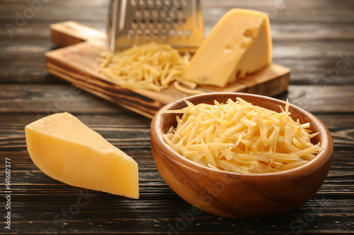 Bowl with grated cheese on wooden table