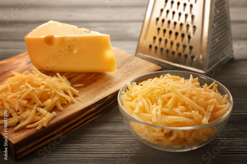Bowl and wooden board with grated cheese on table