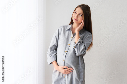 Bild auf Leinwand Beautiful pregnant woman standing near window at home