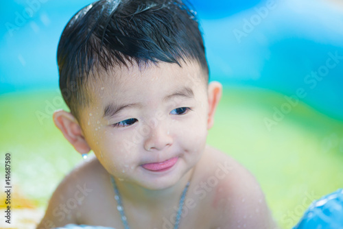 Asian kid playing in inflatable baby swimming pool on hot summer day.
